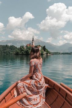 a woman is sitting in a boat on the water looking out at an island with a church