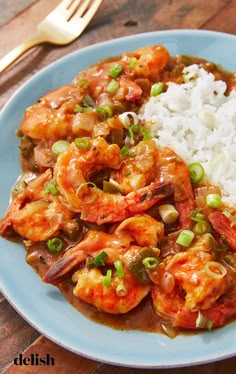 a blue plate topped with shrimp and rice next to a fork on a wooden table