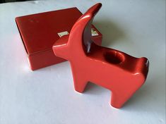 a red dog shaped object sitting on top of a white table next to a box