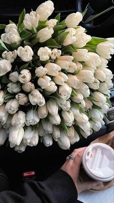 a bouquet of white tulips sitting on top of a table next to a cup