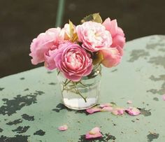 pink flowers are in a glass vase on an old table with petals scattered around it