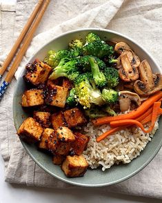 a bowl filled with rice, broccoli and tofu next to chopsticks