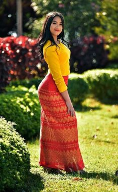 a woman is standing in the grass wearing a long red skirt and yellow shirt with her hands on her hips