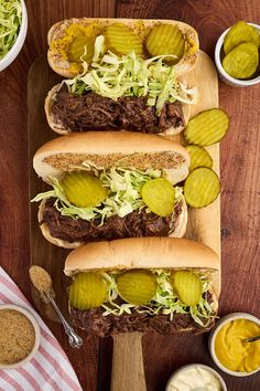 three hot dogs with pickles and mustard on a cutting board