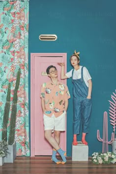 two people standing next to each other in front of a blue wall with cactus plants