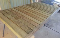 a wooden table sitting on top of a cement floor next to a white car in the background