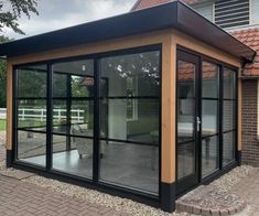 a small house with glass walls and doors on the outside, in front of a brick building