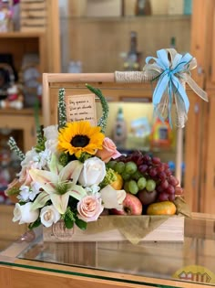 a bouquet of flowers and fruit in a wooden box on a table with a blue ribbon