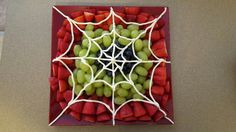 grapes and strawberries are arranged in a spider web pattern on a red plate with white string