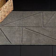 a woven basket sitting on top of a floor next to a gray rug with an arrow pattern