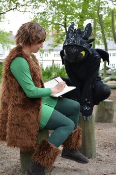 a woman sitting on top of a tree stump next to a dragon statue with a notebook in her hand