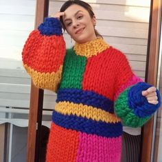 a woman wearing a multicolored knitted sweater and holding her hand on her head