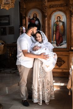 a man and woman holding a baby in front of a church with paintings on the walls