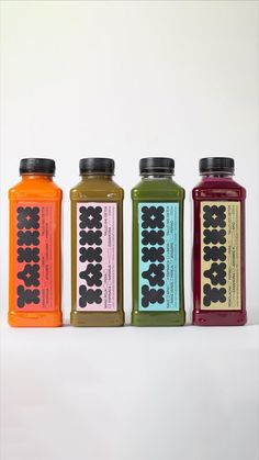 four bottles of juice are lined up on a white surface, each containing different colors