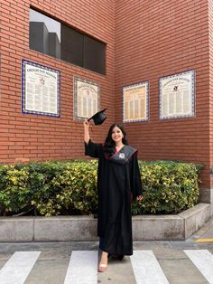 a woman wearing a graduation gown and holding up her diploma in front of a brick building