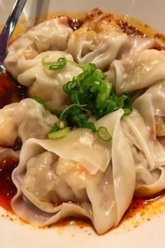 a white plate topped with dumplings covered in sauce and garnished with green onions