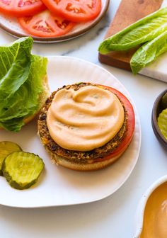 a plate with a sandwich on it next to some pickles and tomato slices in bowls