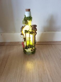 an illuminated bottle with plants growing out of it sitting on a wooden floor next to a wall