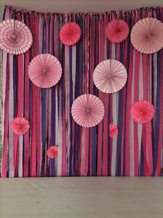 pink and purple paper umbrellas are hanging on the wall next to streamers in front of a curtain