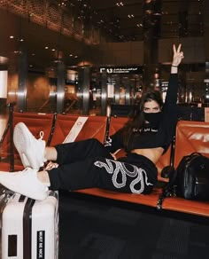 a woman sitting on top of a bench next to an airport luggage bag with her hand up in the air