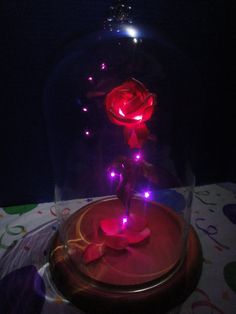 an illuminated rose under a glass dome on a table