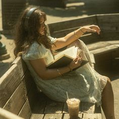 a woman is sitting on a bench reading a book and holding a drink in her hand