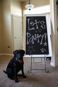 a black dog is sitting in front of a chalkboard that says let's party