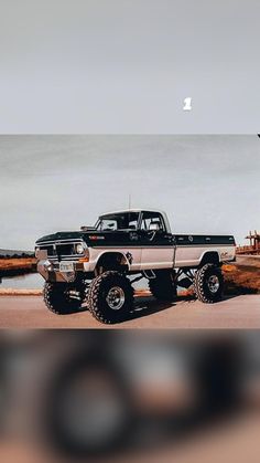 an old black and white truck parked in front of a lighthouse on the ocean shore