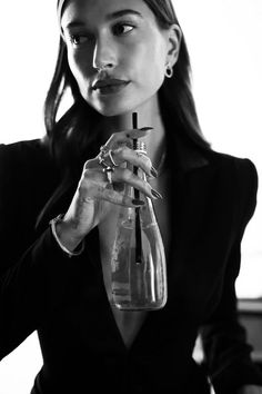 a woman in a black suit holding a clear bottle with red nail polish on it