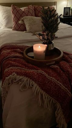 a lit candle on a tray in the middle of a bed with blankets and pillows