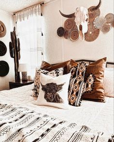 a bed topped with lots of pillows next to a wall mounted cow skull on the wall