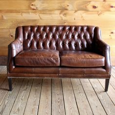 a brown leather couch sitting on top of a hard wood floor next to a wooden wall