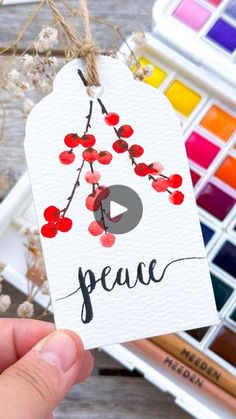 a person holding up a card with the word peace written on it next to some watercolors