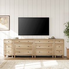 a living room with a large tv mounted on the wall next to a dresser and potted plant