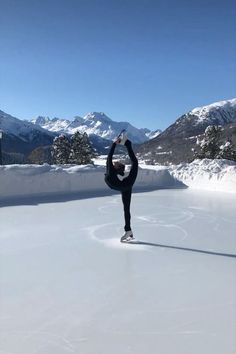 a person standing on one leg in the middle of an ice skating rink with mountains in the background