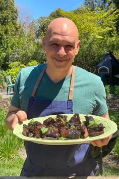 a man holding a plate with food on it in front of some bushes and trees