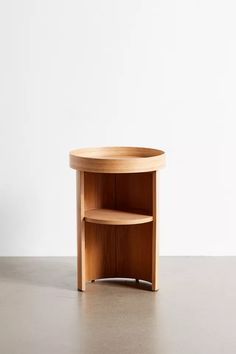 a round wooden table sitting on top of a cement floor next to a white wall