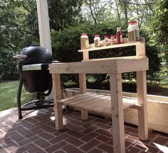 an outdoor bbq grill on a brick patio next to a wooden bench with barbecue tools