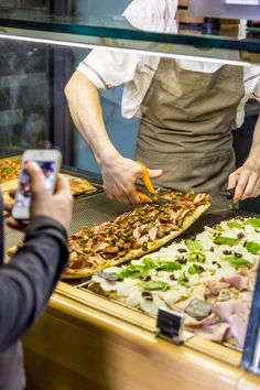 two people are taking pictures of pizzas in a display case at a restaurant while another person takes a photo