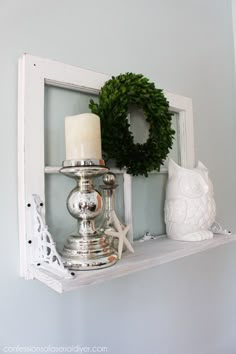 a white shelf with candles and wreath on it