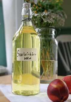 a bottle of liquid sitting on top of a table next to two apples and flowers