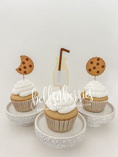 three cupcakes with icing and cookie toppers sitting on small white plates