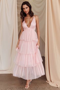 a woman wearing a pink dress standing in front of curtains