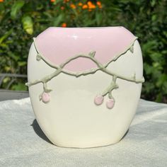 a pink and white vase sitting on top of a table next to some trees in the background