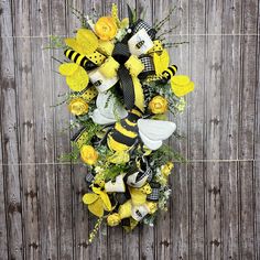 a yellow and black wreath with bees, roses, and flowers on it against a wooden wall