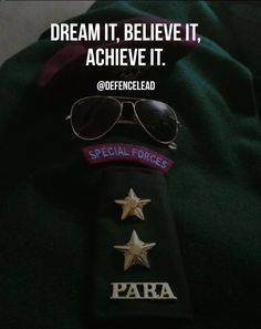 a hat, sunglasses and some badges on top of a green shirt with the words dream it believe it achieve it