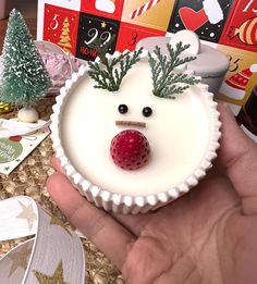 a hand holding a cupcake with a face on it and a berry in the middle