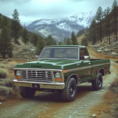 a green truck parked on the side of a dirt road in front of some mountains