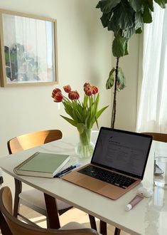 a laptop computer sitting on top of a white table next to a vase with flowers