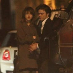 a man and woman standing next to each other in front of a car at night